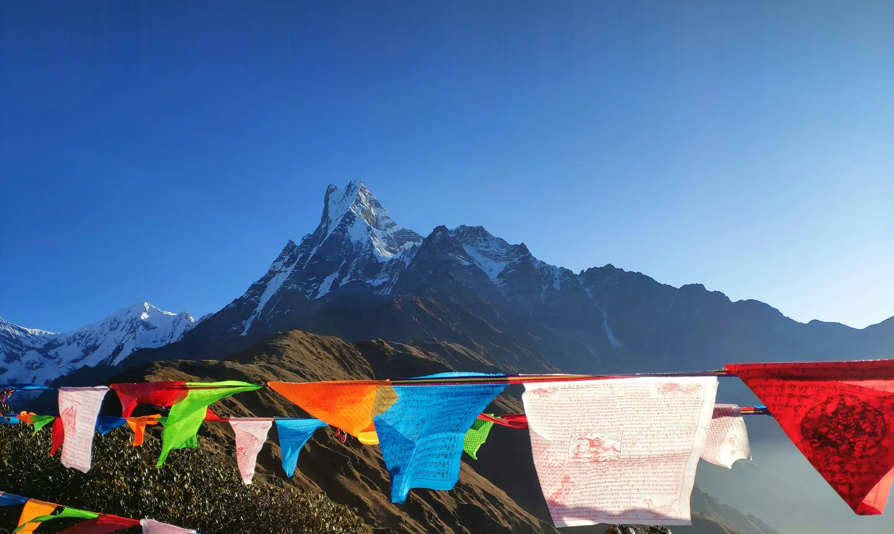Prayer flags in front of a snow-capped Himalayan peak under a clear blue sky